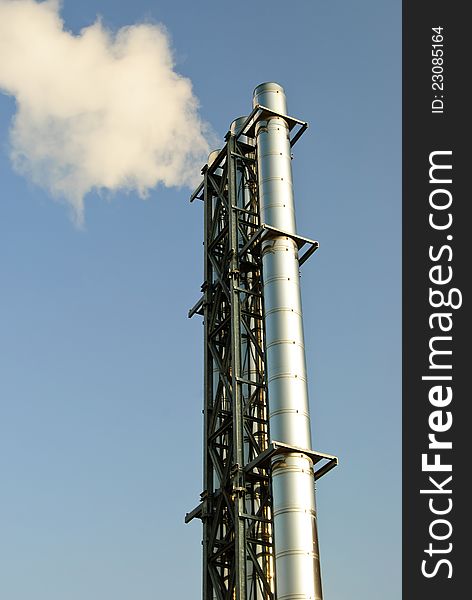 Vertical shot of industrial chimney with grey smoke on blue sky. Vertical shot of industrial chimney with grey smoke on blue sky.