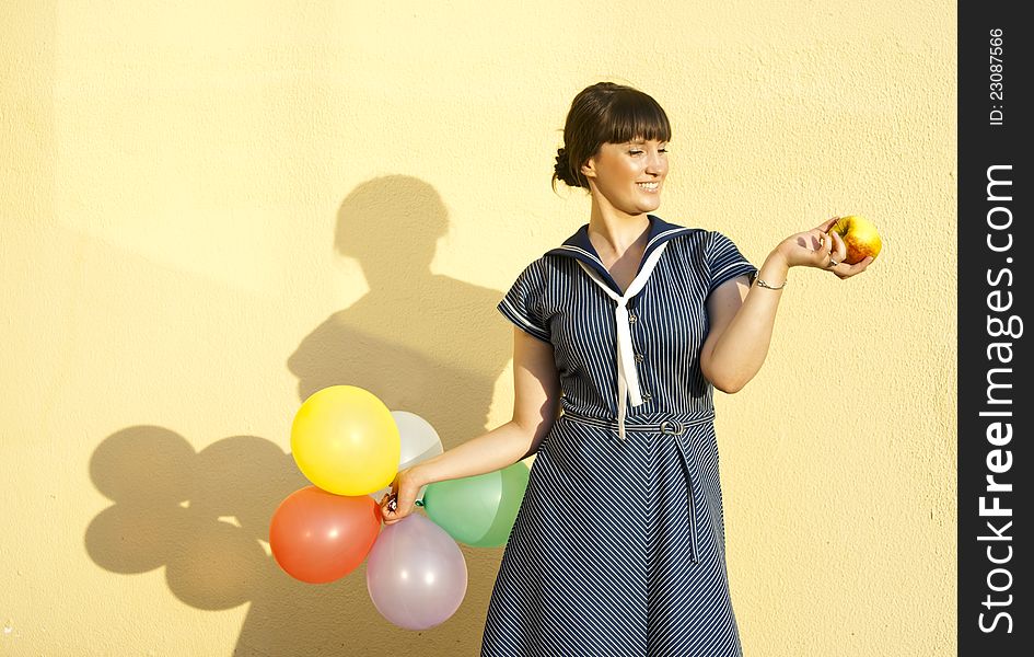 Beautiful happy girl on the background of the wall keeps apple and balloons. Beautiful happy girl on the background of the wall keeps apple and balloons