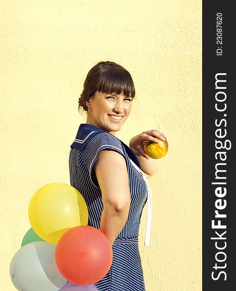 Beautiful brunette girl on the background of the wall keeps apple and balloons. Beautiful brunette girl on the background of the wall keeps apple and balloons