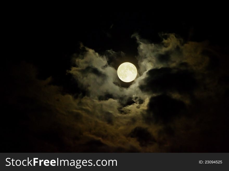 Full moon can be seen through scattered clouds in the night sky.