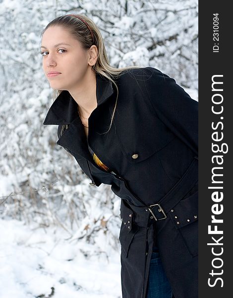 Young girl in winter park in black raincoat. Young girl in winter park in black raincoat