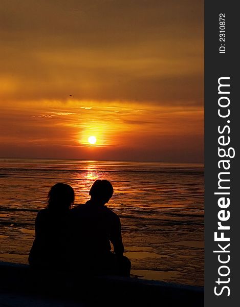 Couple sitting at sea side watching sun set . Couple sitting at sea side watching sun set .