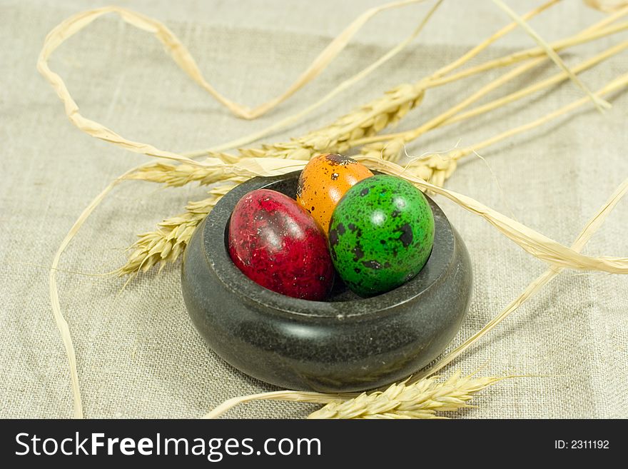 Colorful eggs in bowl and wheat ears