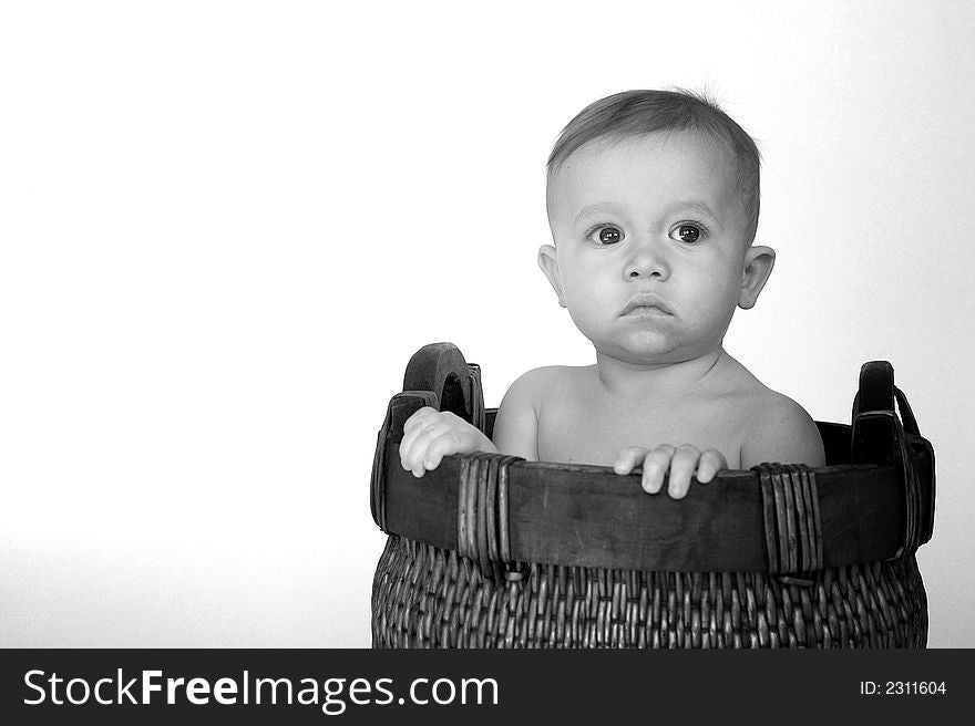 Black and white image of cute baby sitting in a woven basket. Black and white image of cute baby sitting in a woven basket