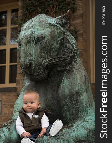 Image of cute baby sitting in front of a lion sculpture. Image of cute baby sitting in front of a lion sculpture