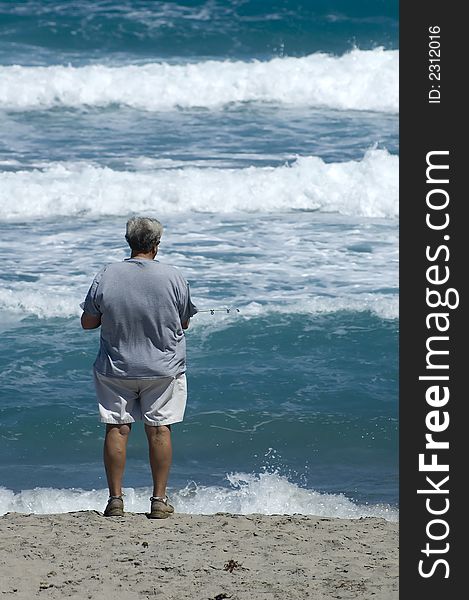 Man fishing in the surf with waves in background. Man fishing in the surf with waves in background