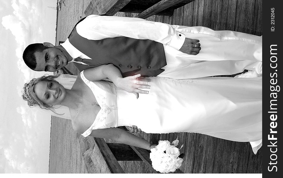 A bride and groom standing on a boardwalk with brides hand extended showing off her new ring in black and white, ring is glowing. A bride and groom standing on a boardwalk with brides hand extended showing off her new ring in black and white, ring is glowing.