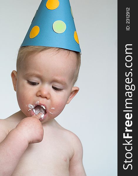 Image of an adorable 1 year old, wearing a paper hat, eating birthday cake. Image of an adorable 1 year old, wearing a paper hat, eating birthday cake