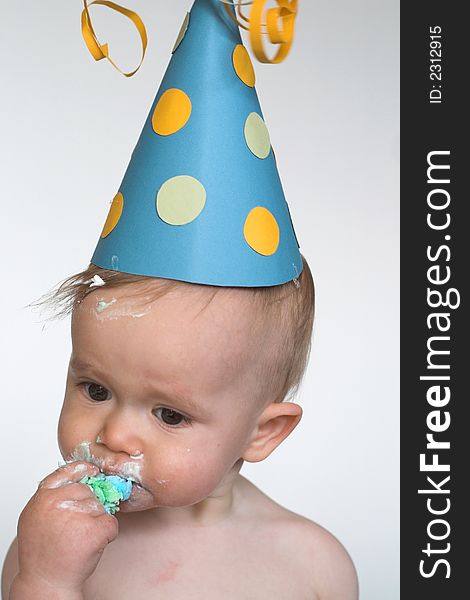 Image of an adorable 1 year old, wearing a paper hat, eating birthday cake. Image of an adorable 1 year old, wearing a paper hat, eating birthday cake