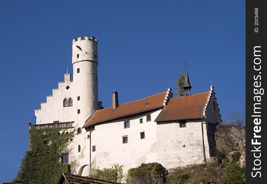 White castle with tower and main house in front of blue sky