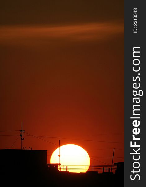 Darkly-purple sunset of a sun above the roofs of houses.