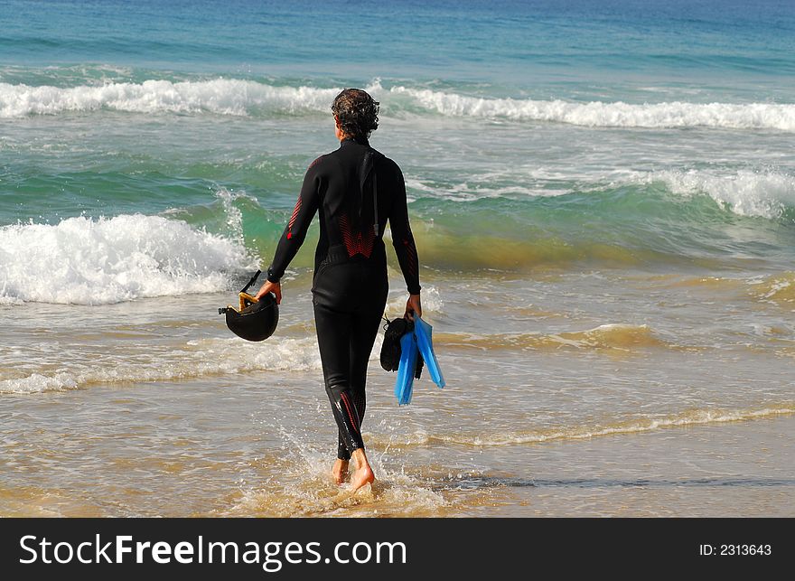 Surfer Standing in the water looking at the surf with helmet and flippers in his hands. Surfer Standing in the water looking at the surf with helmet and flippers in his hands