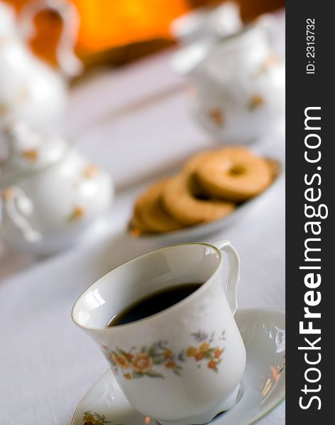 Coffee set on the table - cup of coffee on the front (shallow DOF focus on the liquid edge) cookies and milk jug, sugarl bowl behind.