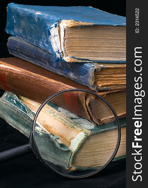 Old books and magnifier on a black background