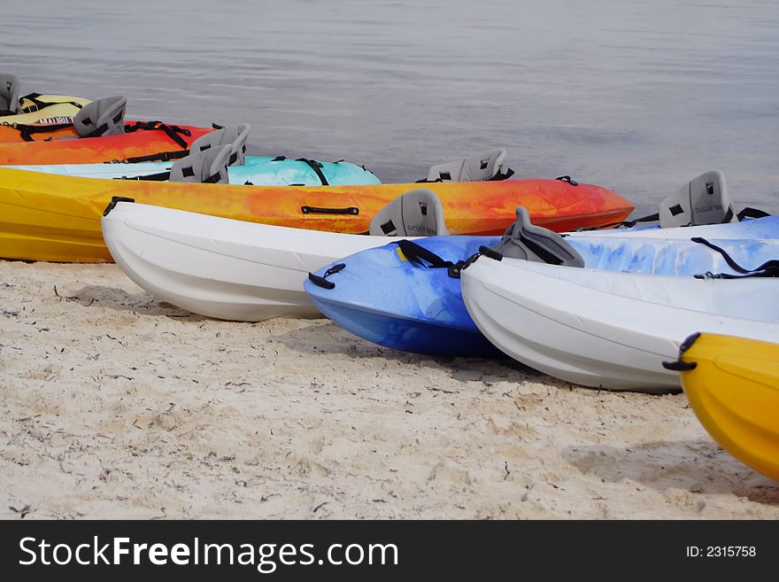 Colorful sea kayaks lined up on a sandy ocean shore.