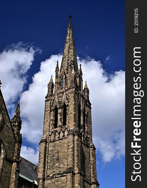 Old stone church steeple reaching up into the deep blue sky in front of clouds