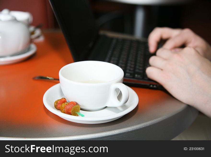 Cap of tea, hands and netbook on the table in cafe. Cap of tea, hands and netbook on the table in cafe