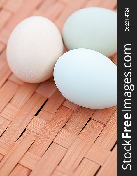 Close shot of three colorful organic eggs sitting in a cluster on a basket.