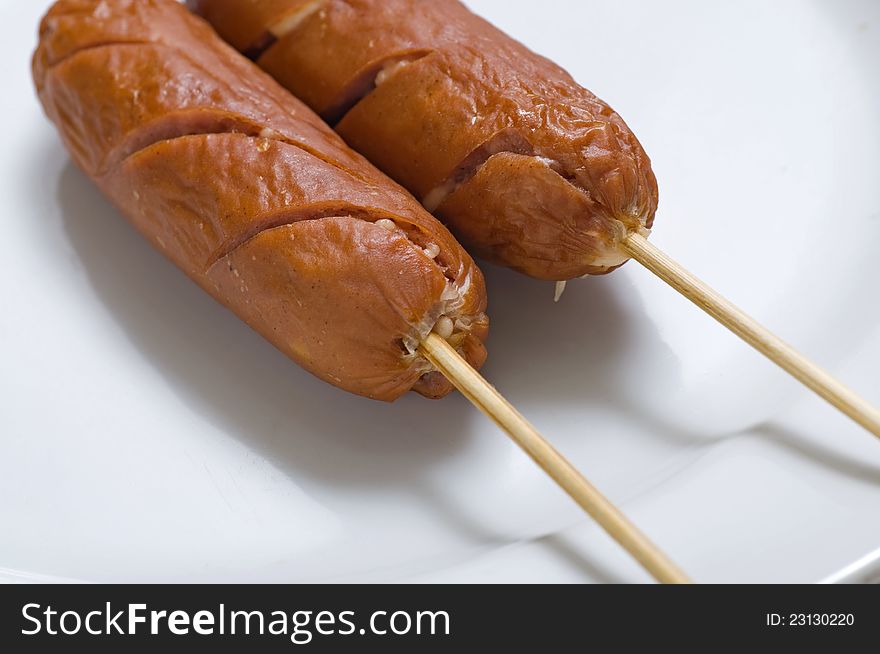 Two sausages on the white dish, serve with wooden stick