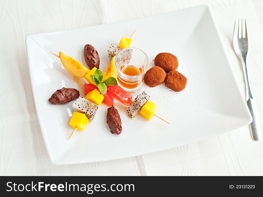 A fine fruit salad dessert on white plate with chocolate truffles and caramel sauce. A fine fruit salad dessert on white plate with chocolate truffles and caramel sauce.
