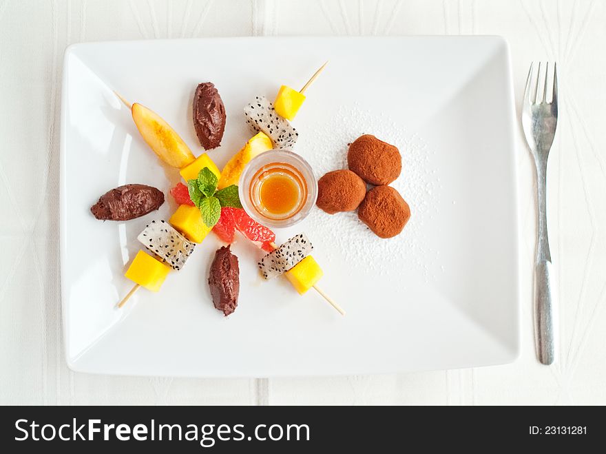 A top view of a fruit salad dessert on white plate with chocolate truffles and caramel sauce. A top view of a fruit salad dessert on white plate with chocolate truffles and caramel sauce.