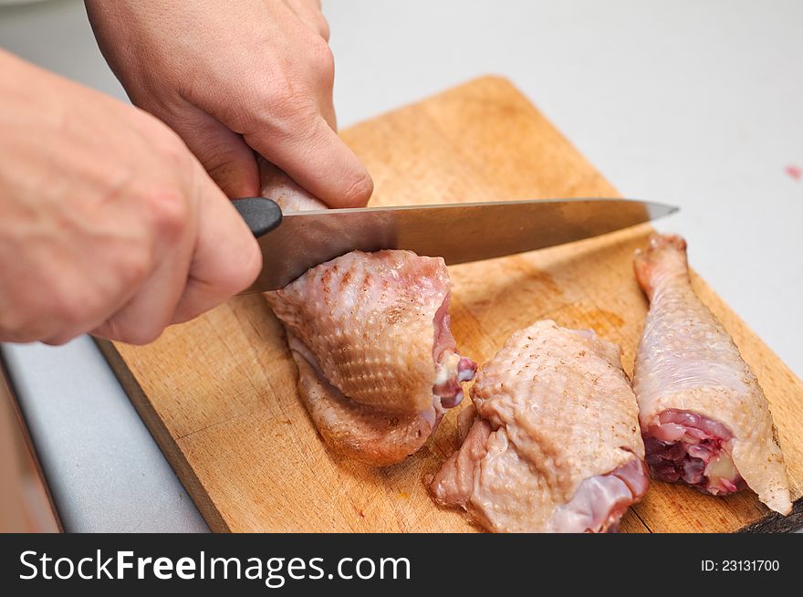 A chef cutting chicken leg for cooking with other pieces. A chef cutting chicken leg for cooking with other pieces.