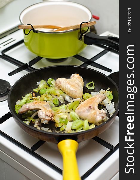 Frying chicken wings and leek on a pan.