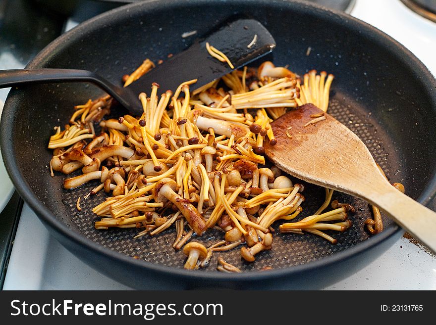 Enoki and shimeji mushrooms frying on a pan.