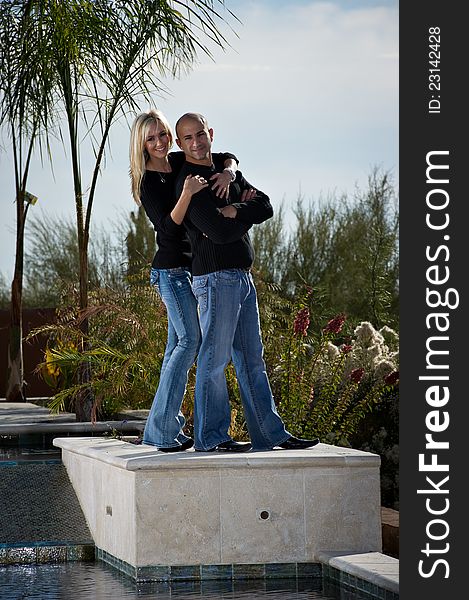 Full length of a happy playful couple posing next to a pool. A green winter desert landscape is in the background. Full length of a happy playful couple posing next to a pool. A green winter desert landscape is in the background.