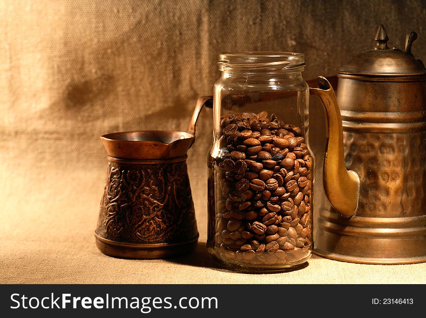 Glass jar with coffee beans near old copper coffeepot on canvas background. Glass jar with coffee beans near old copper coffeepot on canvas background