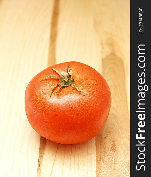 A red ripe tomato with stem on a wood cutting board. A red ripe tomato with stem on a wood cutting board