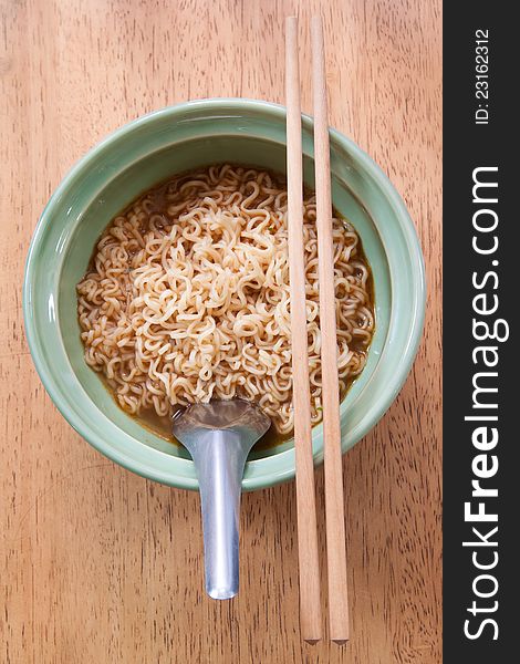 Instant noodle with spoon and chopsticks in a ceramic bowl on wood background