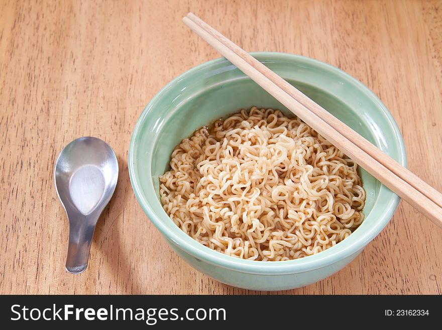 Instant noodle with spoon and chopsticks in a ceramic bowl on wood background