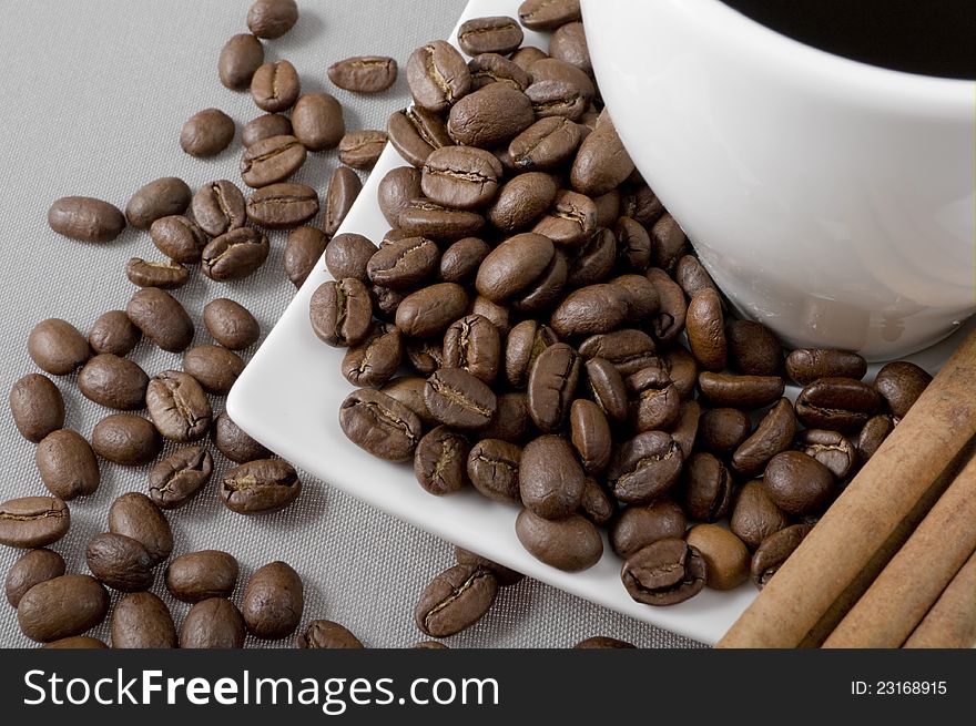 Black coffee, grains and cinnamon on a grey background