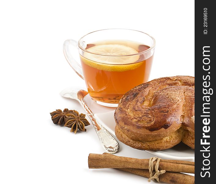 A roll with a cinnamon lies on a background an black tea with a lemon and spices on a white background. A roll with a cinnamon lies on a background an black tea with a lemon and spices on a white background