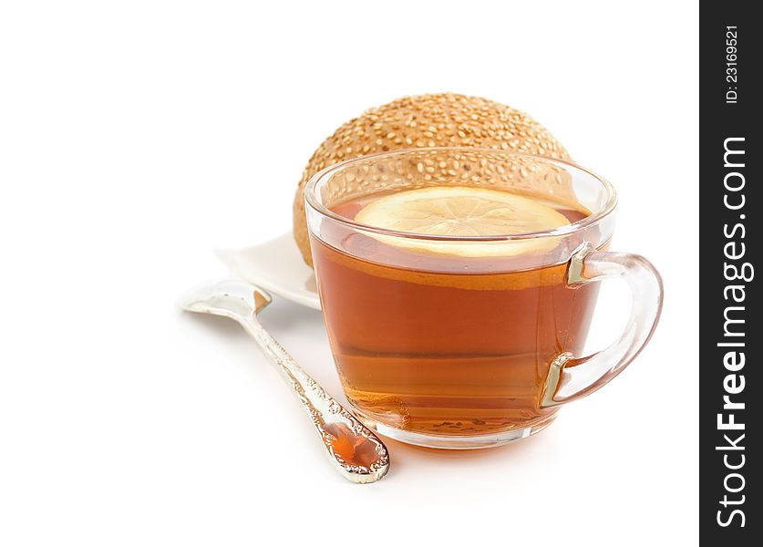 Cup of black tea with a lemon, tea spoon and roll with sesame on a white background