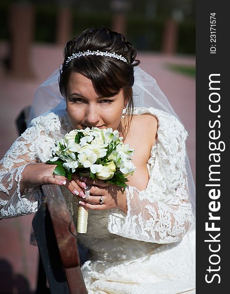 Happy bride sits on bench in park