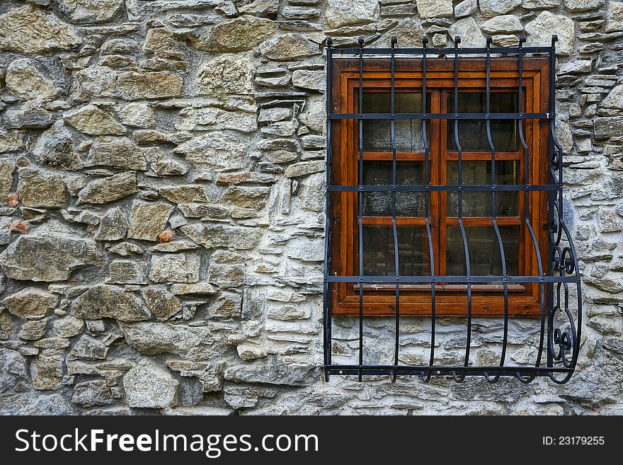 Stone wall with window enclosed in wooden frame and steel ornamental grillage on it. Stone wall with window enclosed in wooden frame and steel ornamental grillage on it