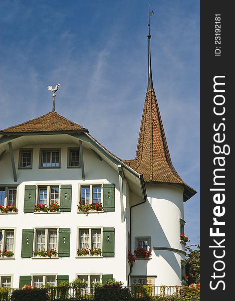 Facade of a Swiss house with green shutters and a circular tower topped with a spire