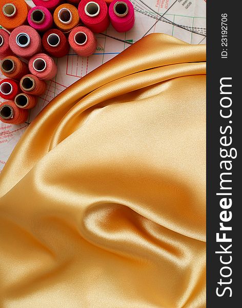 Few colored bobbins and golden silk on sewing pattern