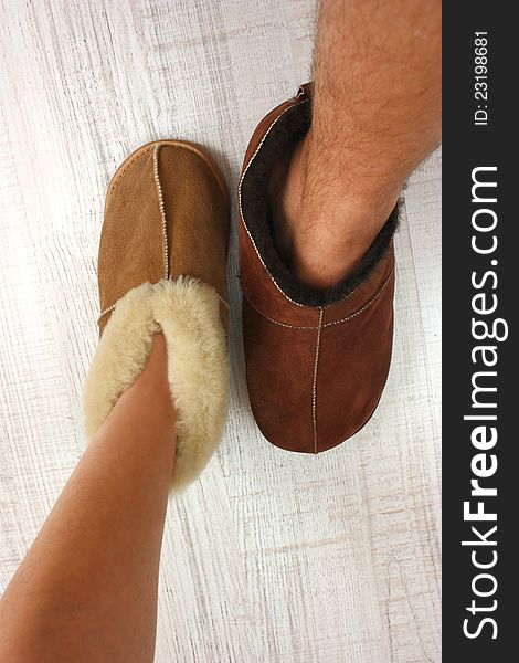 A male and female feet ware warm slippers on a white floor. A male and female feet ware warm slippers on a white floor