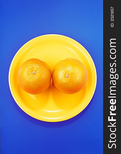 Two orange tangerines in  bright, yellow plate on dark blue background