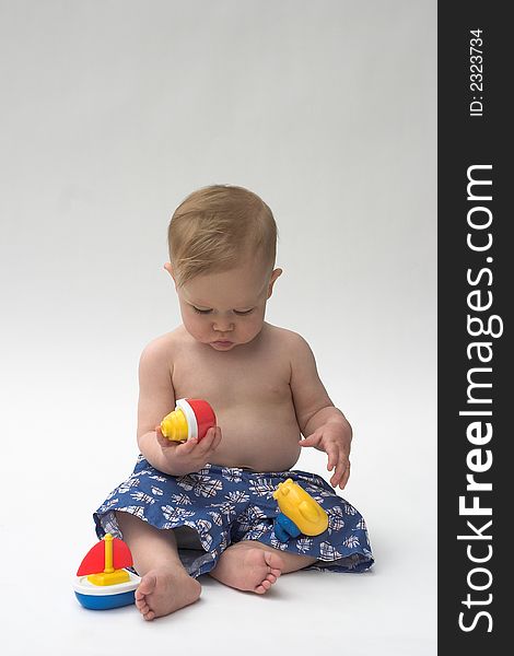 Image of an adorable baby wearing shorts, playing with toy boats. Image of an adorable baby wearing shorts, playing with toy boats