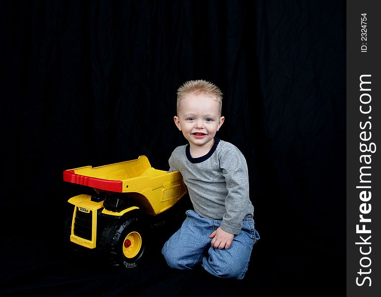 Cute little boy on black background with his truck