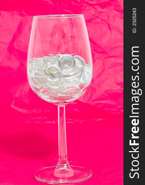 Sparkling stones in a wine glass on a red background. Sparkling stones in a wine glass on a red background