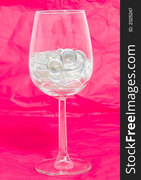 Sparkling stones in a wine glass on a red background. Sparkling stones in a wine glass on a red background