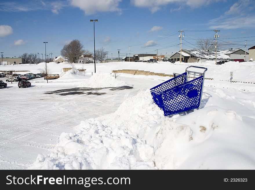 A shopping cart stuck at the top of a high snowbank by a retail parking lot. A shopping cart stuck at the top of a high snowbank by a retail parking lot.