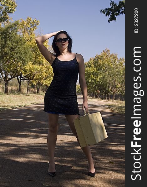 Brunette waiting with her suitcase and black dress next to road. Brunette waiting with her suitcase and black dress next to road