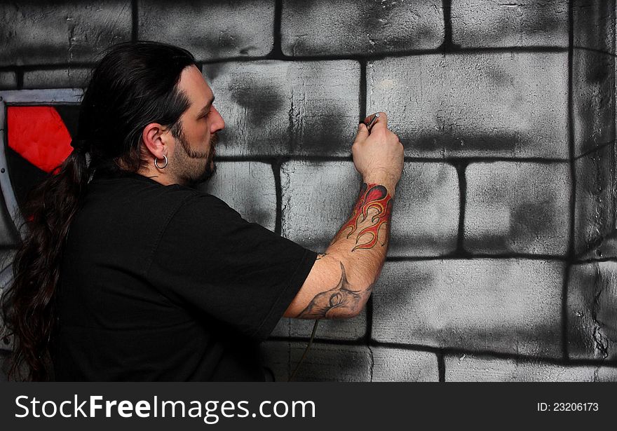 A man with tattoos make drawing on a wall painting bricks. A man with tattoos make drawing on a wall painting bricks