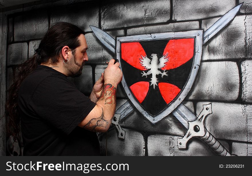 A man with tattoos make drawing on a wall painting knight shield. A man with tattoos make drawing on a wall painting knight shield